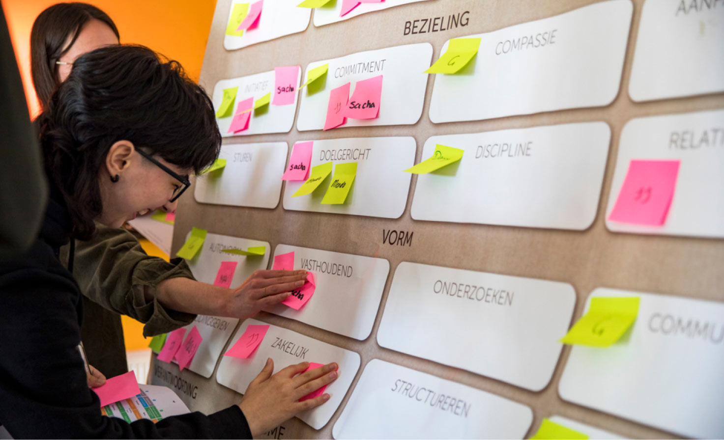 Een foto van Maijla die glimlacht terwijl ze een post-it note plaatst op een bord over teamsdynamiek.